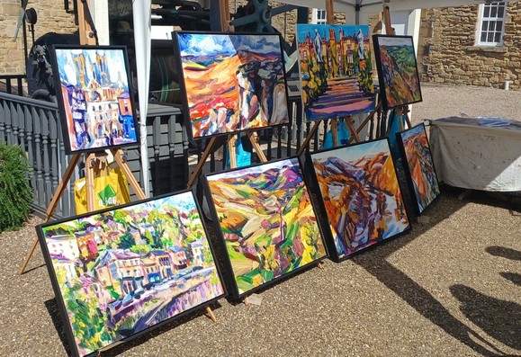 A display of large, vibrantly coloured artworks on easels in a sunny courtyard