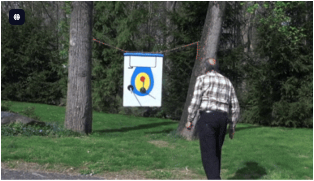 A person in a plaid shirt throws a toilet plunger toward a target mounted between trees in a park setting, with the plunger's trajectory traced by a red dotted line showing its parabolic path through the air.