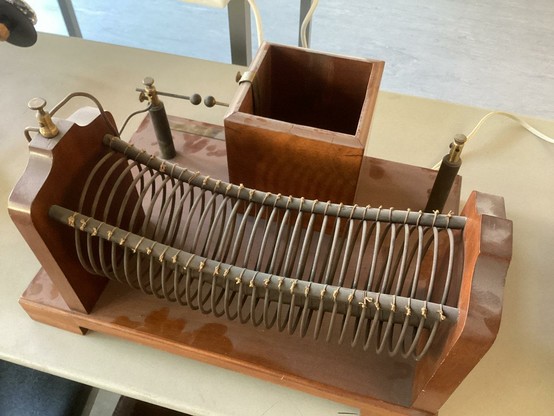Physikalisches unbekanntes Experiment.
In einem hölzernen Aufbau ist eine sehr locker gewickelte Spule und ein Holzkasten, auf dessen Boden sich Alufolie befindet.