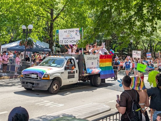 A truck decorated in Pride flags touts a signs that say "We Stand with LGBTQ Immigrants / ICE Go Home!" and "Queer Rights = Workers' Rights."