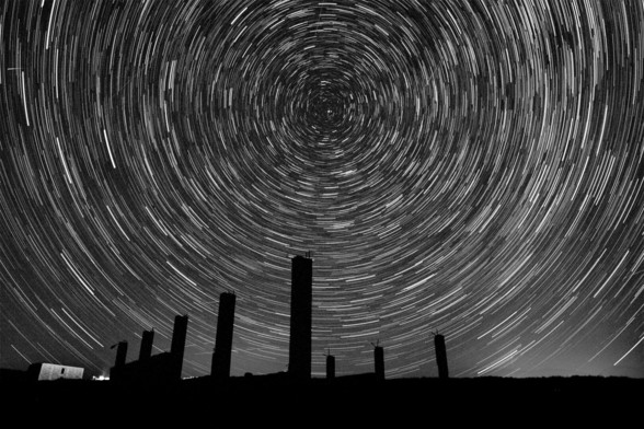 Black and white photograph showing the silhouettes of the columns of a building at the bottom of the photo and above them a circumpolar star cluster.