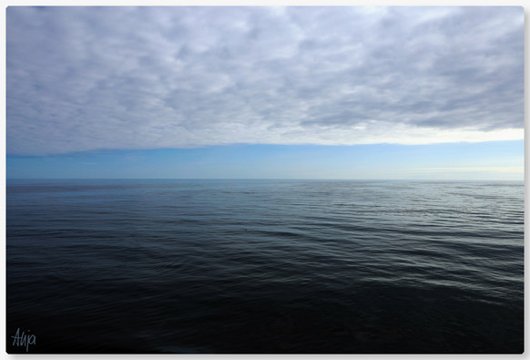 Eine dichte Wolkendecke aus vielen kleinen Wölkchen am Himmel über dem Atlantik, darunter ein blauer wolkenloser Streifen über dem leicht bewegten Meer. Sonnenlicht fällt am rechten Bildrand durch die Wolken auf das Wasser und betont die leichten Wellen.

A dense cloud cover consisting of many small clouds in the sky over the Atlantic, below a blue, cloudless strip over the gently moving sea. Sunlight falls through the clouds onto the water at the right-hand edge of the picture, emphasising the gentle waves.