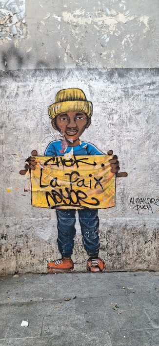 Peinture au spray de 2m de hauteur representant un homme racisé brun habillé chichement baskets oranges jean plissé et veste de survêtement bleu clair à bandes blanches il tient un tissu jaune orange de 80cm sur 40 cm sur lequel est inscrit au spray noir en fines lettres cursives La Paix c'est signé hors cadre sur la droite au Posca noir en cursives Alenxandre Puga.

2 gros nazes on tomé en haut et en bas de La Paix leurs blazes de ploucs Chek et Nayor