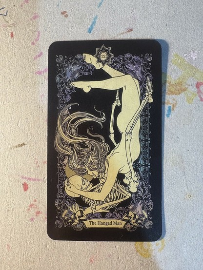 A tarot card featuring a skeleton and a naked woman lying in each others arms and sharing an emotional look