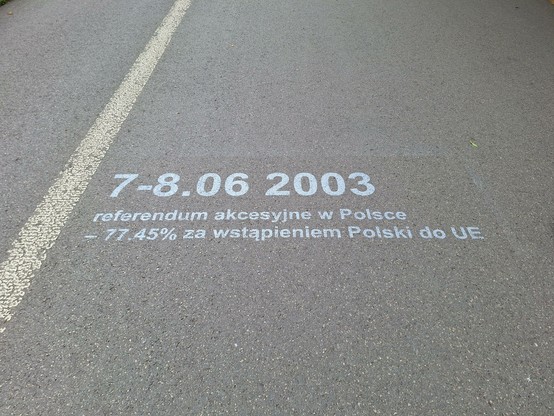 Picture showing a bike lane or pedestrian walkway with the following printed on it:
7-8.06. 2003
referendum akcesyjne w polsce - 77.45% za wstapieniem Polski do UE

which according to translation programmes means
Accession referendum in Poland - 77.45 in favour of Poland joining the EU

[if not, this could be pretty awkward :D :D ]