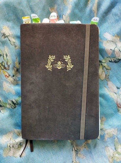 Cover of Midsummer Night themed journal from Notebook Therapy. The hardcover is brown velvet with a gilded bee and plants on it. The top is lined with budgie shaped bookmarks.