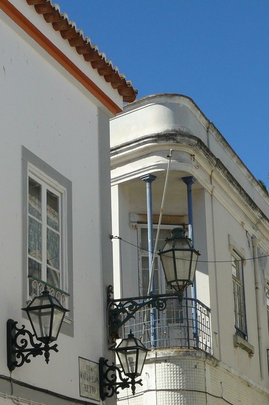 A imagem mostra as esquinas muito próximas de dois edifícios de dois pisos, do início do século XX, pintados de branco, numa rua estreita. À esquerda vê-se uma janela alta, de caixilharia de madeira pintada de branco e seis vidraças que reflectem o edifício defronte. A janela e a esquina tem um friso pintado de cinzento. Na esquina está um candeeiro antigo, com um longo braço, em ferro forjado de cor escura, desactivado. Em cada lado da janela, num plano inferior estão dois candeeiros de ferro forjado, mais pequenos e sem braço, sendo visíveis as lâmpadas no interior. Por baixo,  uma placa em azulejos com o nome "Rua Marreiros Netto".

O edifício da direita  tem a esquina em forma de cunha arredondada, com uma pequena varanda triangular protegida por um gradeamento de ferro forjado escuro . A varanda é suportada por duas colunas de ferro pintadas de azul claro.
O edifício é encimado por uma platibanda com dois frisos escuros escurecidos por manchas de humidade. No topo, uma nesga de céu azul luminoso, sem nuvens.