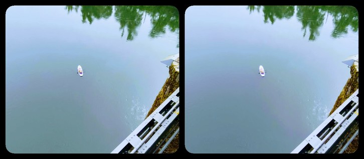 Stereoscopic view. We're looking down some distance from a bridge onto a still river. Near the center of the image is a fisherman in a small boat. Lower right corner, you can see part of the bridge.