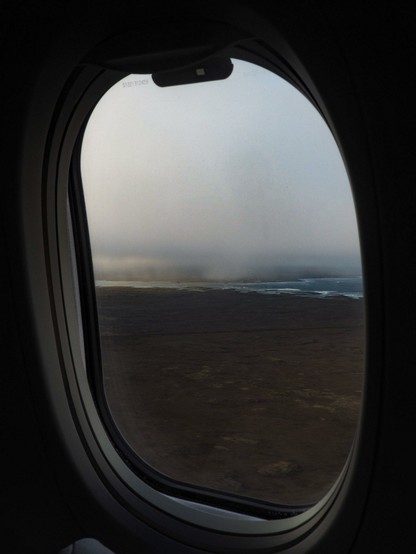 An airplane window with a moody, misty, coastal view.