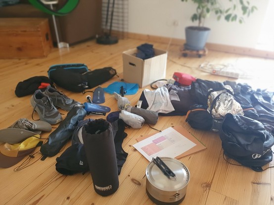 an assortment of camping, hiking and running gear (tent, shoes, backpack, poles, cooking gear ...)spread over floor, waiting to be packed.