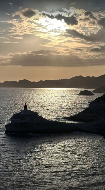 At sunset the steadfast lighthouse perched on rugged rocks, bathed in the warm hues of a stunning sunset reflecting off the beautiful calm sea.