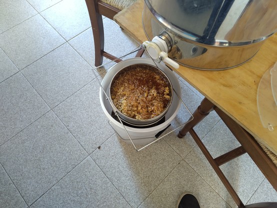 Freshly centrifuged honey being filtered: picture of a honey centrifuge with a sieve below it, and a bucket filling with honey