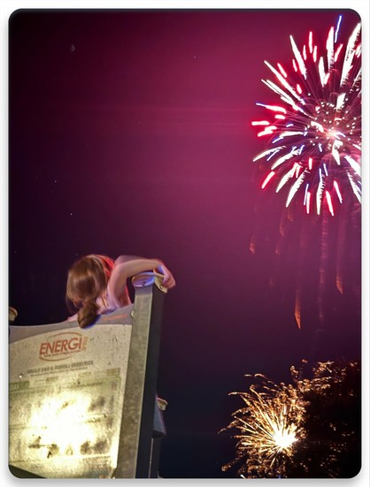 A child looking up towards a darkened pink sky as showers of red white blue &amp; yellow fireworks go off before them.