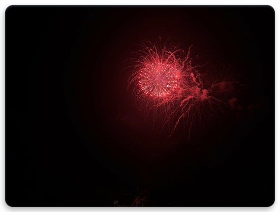 Black night sky with a bright red explosion of fireworks, lighting up the smoke of fireworks before it trailing down to the ground.
