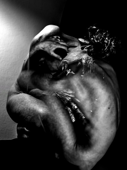 Black and white photo, portrait format, low-key, high-contrast. Multiple exposures. Self-portrait of a squatting woman. Two different poses are exposed one above the other, so that some body parts appear double: hands, arms, back. The woman is unclothed, her hair hangs to one side, her doubtful gaze directed at the viewer, but deep in thought. Her hands are wrapped protectively around parts of her body, the overall impression gloomy, conveying unpleasant thoughts.