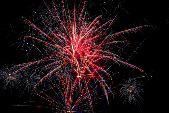 A series of big red fireworks explode and chan ge to a deep blue as the embers fall back to earth.