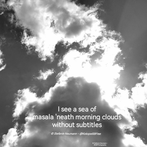 A black and white picture of the sun backlighting fluffy clouds. Beneath a haiku in white letters. Text:

I see a sea of
masala 'neath morning clouds
without subtitles

© Stefanie Neumann - @KokopelliBFree