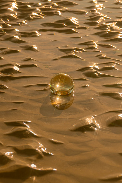 Sphère de verre posée sur le sable mouillé à la golden hour