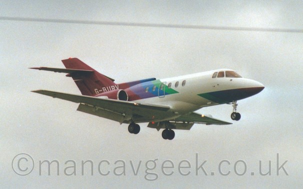 Side view of a twin engined BizJet flying from left to right at a low altitude with flaps extended behind the wings and the undercarriage lowered, suggesting that the plane is about to land.
Coudy grey sky fills the rest of the frame.