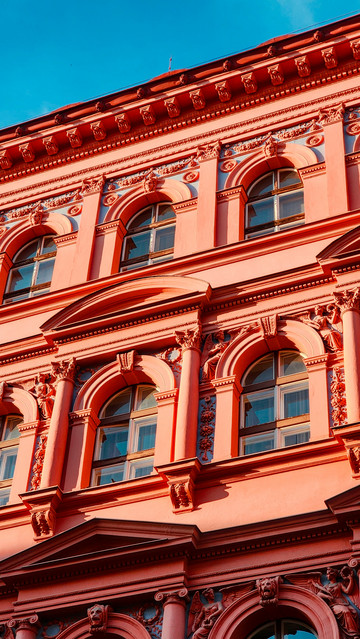 Detail of an impossibly red building with sculptural recesses showing an interplay of light and shadow.