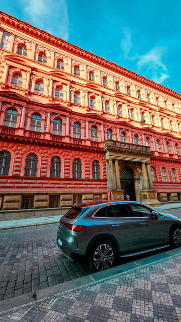 Far shot of an impossibly red building with sculptural recesses showing an interplay of light and shadow contrasting against a powerfully blue sky.