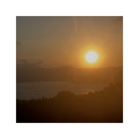 sundown over the hilly coastline of elba, tuscany, italy. the sun looks like a glooming red ball, the hills are already pitch black. far in the distance the mountains are colored in a slightly reddish tone