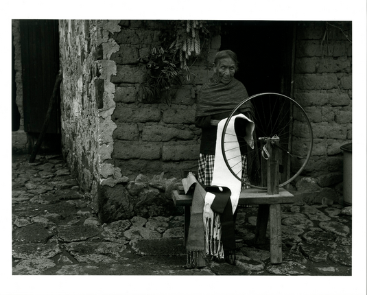 In this black and white photograph a woman stands in front of some kind of spinning device, which uses a bicycle wheel. (It doesn't make sense to me what the wheel is doing in the context of the fabric she's holding. It may be posed and not natural. Still, the tones are amazing, and it's beautiful)