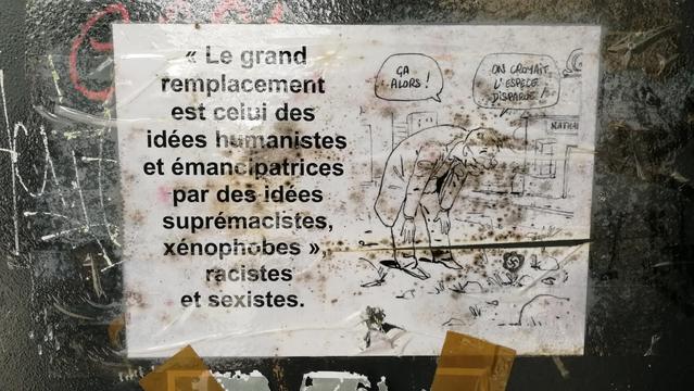 Affiche sur un mur "le grand remplacement est celui des idées emancipatrices par des idées supremacistes, xenophobes, racistes ey sexistes. Un dessin moontre un homme se penchant sur une fleur en forme de croix gammée im dit" ça alors on croyait l'espèce disparue! "