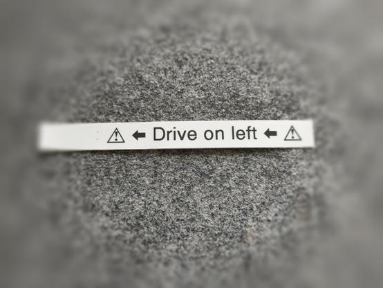 Photo eines selbsterstellten Etiketts mit den Piktogrammen für "Achtung", zwei nach links weisenden Pfeilen und der Aufschrift "Drive on left".