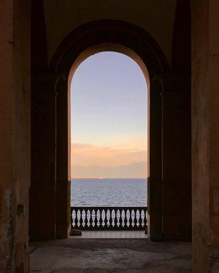 A tall arched window. Sunset at the sea.