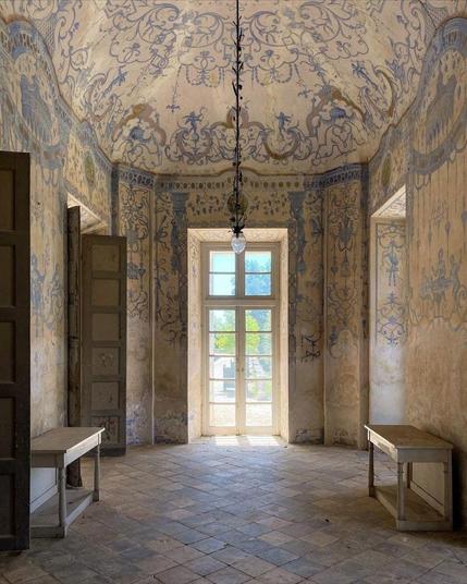 An oval shaped room with tall doors and windows. The walls and the ceiling are covered in white and light blue ornaments.