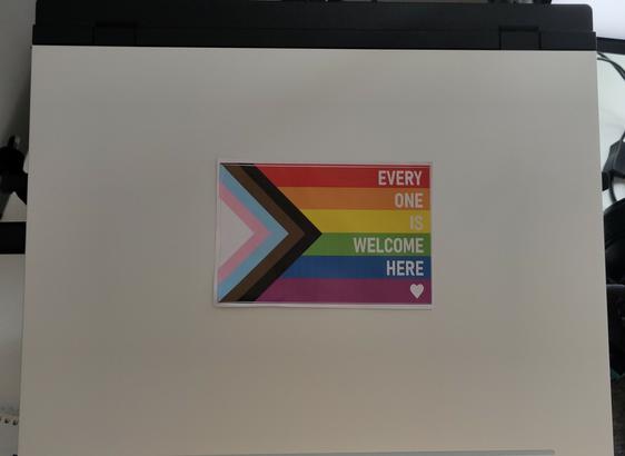 After: Backside of my FrameWork 16 Laptop, but the FrameWork Logo is covered with an sticker, which shows the progressive pride flag, written on "every one is welcome here".