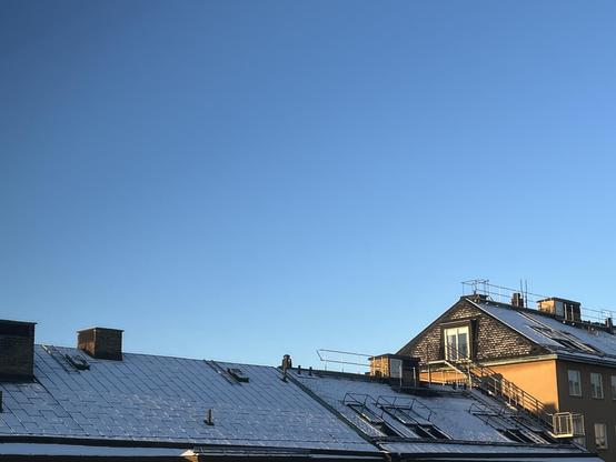 Snowy rooftop skyline, luminous clear blue skye gradient towards white at horizon, Stockholm february 2026.