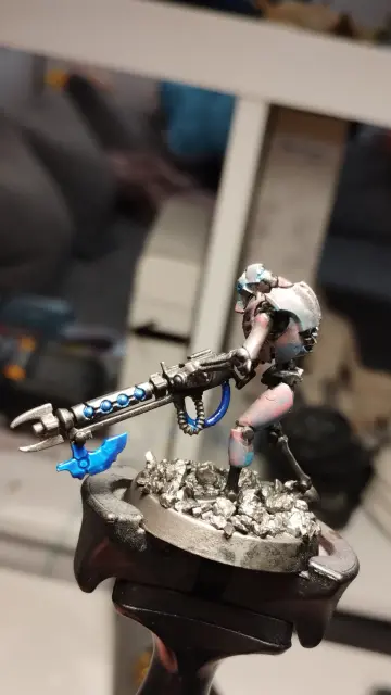 Necron warrior with a black gauss flayer looking to the left.
It has a metallic armor which turns from blue to pink.
The energy highlights on the weapon are a bright blue.