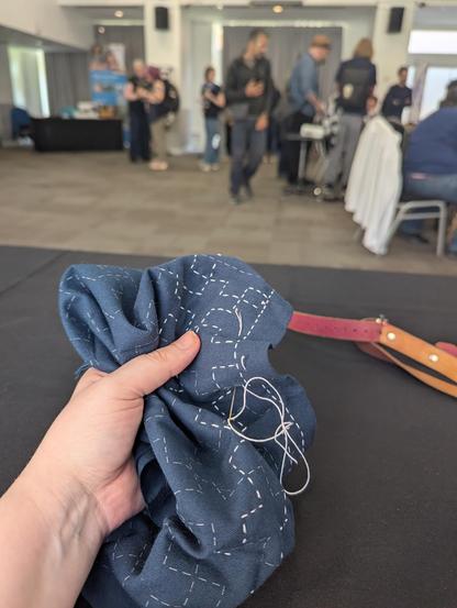 Cat is stitching long straight, visible running stitches into indigo cotton fabric, in a technique known as Sashiko. The raised pattern is in the form of large uniform crosses across the whole cloth. The piece measures about 1ft/30cm when finished.