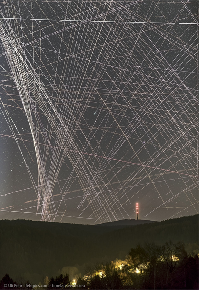 A picture of the night sky completely full of satellite streaks criss-crossing at random angles across the whole image, to the point that it's hard to see a comet or any stars behind the streaks.
