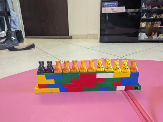 A row of 12 Duplo baby cats (their back to us) sitting atop a wall of Duplo bricks 4 bricks high as if they're standing guard.