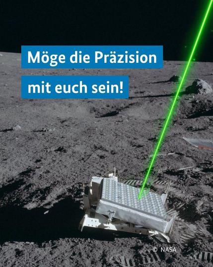 Aufnahme der Mondoberfläche mit einem flachen Reflektor im Vordergrund. Ein grüner Laserstrahl trifft darauf. Darüber steht der Text „Möge die Präzision mit euch sein!“.
