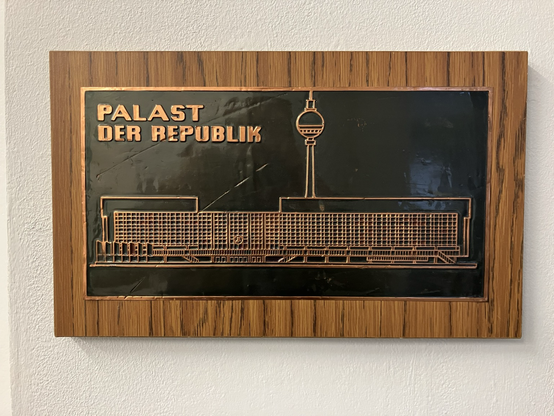 Ein Holzschild mit einem Metallbild des ehemaligen „Palast der Republik“ in Ostberlin
