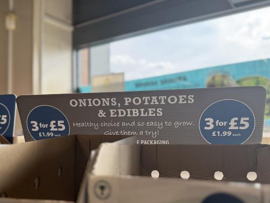 A price sign on a display of seeds, reads “onions, potatoes and edibles”.