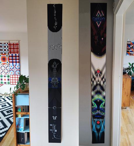 Photo of two long ASCII-prints hanging on a wall, with patchworks visible in the background on two other walls.