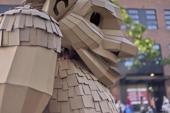 a tight photo of a parade marcher in profile facing right dressed in a large troll costume made from cardboard. Under the head behind the chin the bare face of the marcher can just be made out