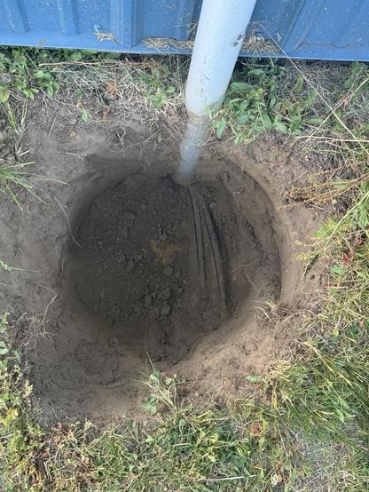 A hole in the dirt, blue metal corrugated structure up top with a conduit that abruptly ends in the hole and some cables protrude out of it. The ground where it’s undisturbed is dry and grassy