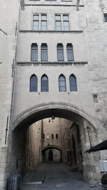 An arch through a wall with a lot of gothic Windows, leaning to another arch  with cobblestones