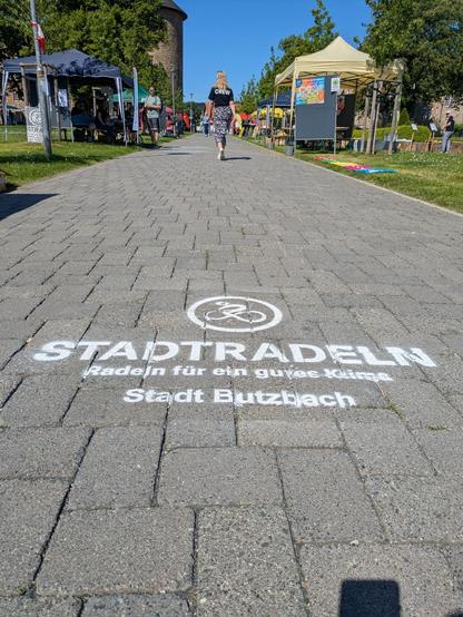 Werbung auf dem Gehweg für das Stadtradeln. Um den Weg herum stehen
einige Stände Demokratiefest.