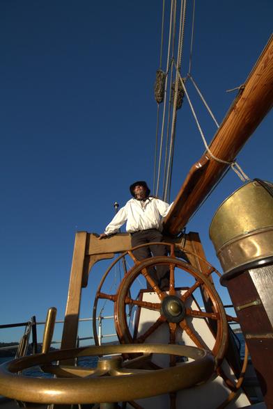 capitaine sur un bateau à voile en hauteur. Il est comle perché au dessus de son gouvernail.
prise de vue extra grand angle