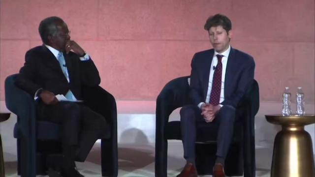 Video clip of two men in suits sitting in what appears to be a stage / interview setting. The man on the right is speaking.