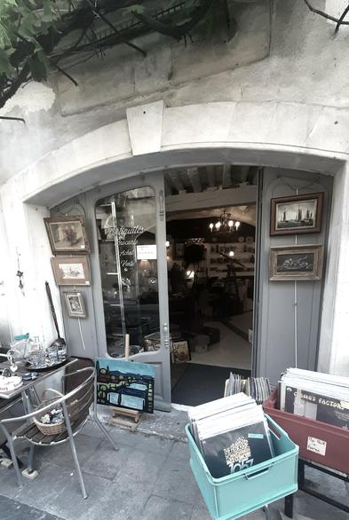 Picture of a shopfront, built into an arch of an old house. It opens the view into an antique shop, with some lights in the gloomy interior. Some merchandise is set up open air to lure in potential shoppers
