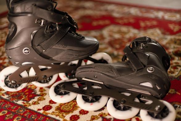 a pair of black K2 inline skates with new white wheels are arranged on a red oriental pattern carpet