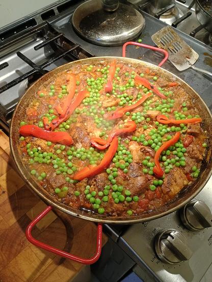 A big paella pan. It's full of paella. Red pepper strips and peas on top, to give it some color.